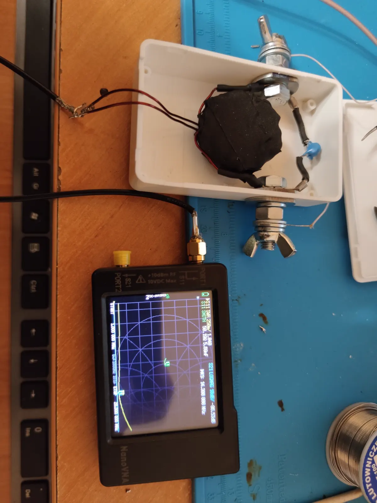 The box connected to a NanoVNA through an adapter, S11 and a Smith chart on the screen